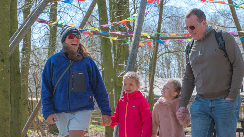 A family of 4 with walking through woodland at Cotswold Farm Park on an Easter egg hunt