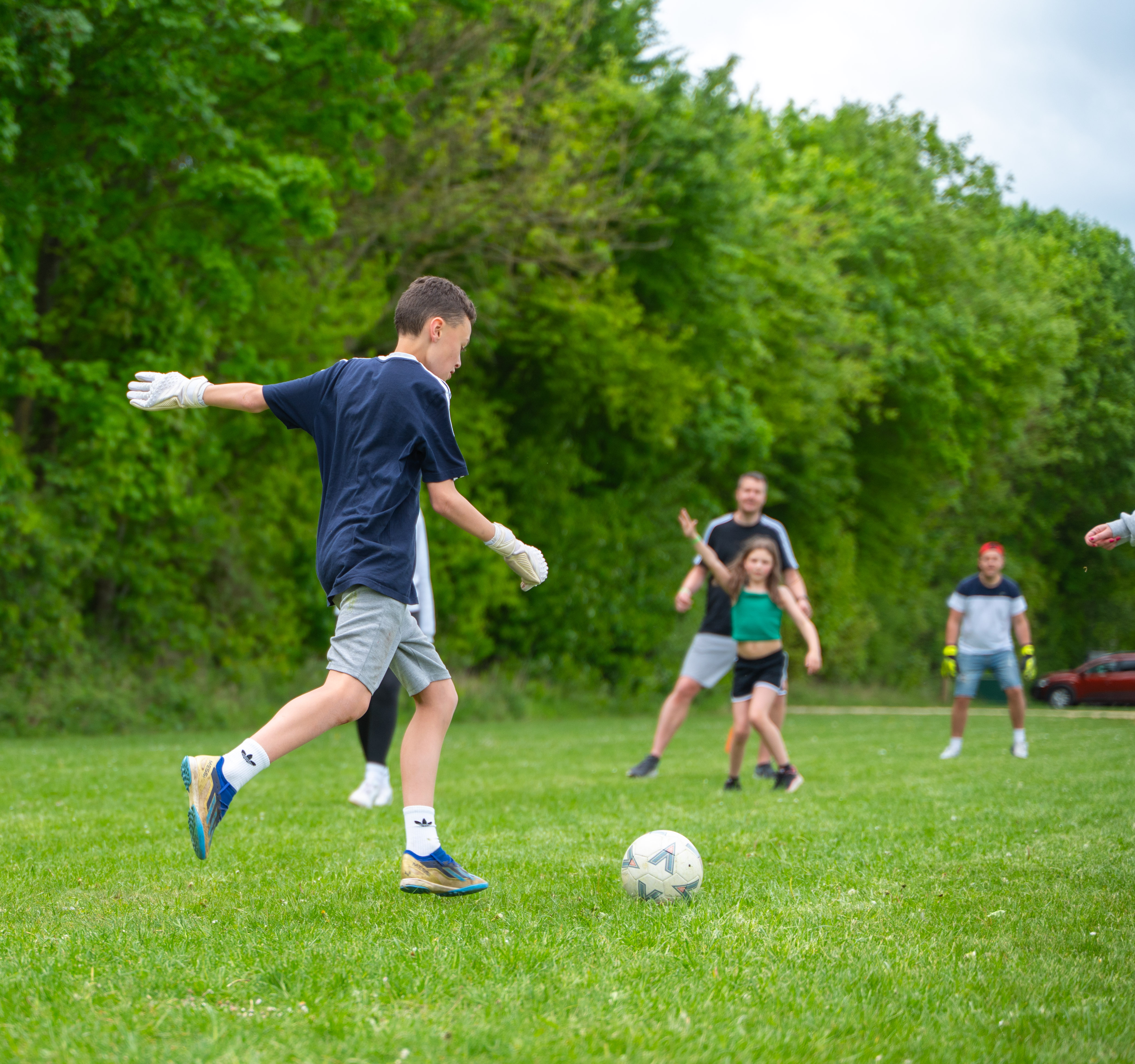 A group of families playing football on the recreation field at Cotswold Farm Park Holidays, where a teenage boy is gearing up to kick.