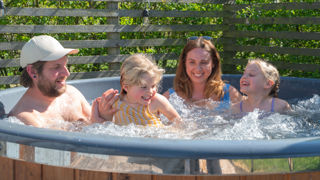 A family of 4 with two young girls splashing in a hot tub at a lodge at Cotswold Farm Park Holidays