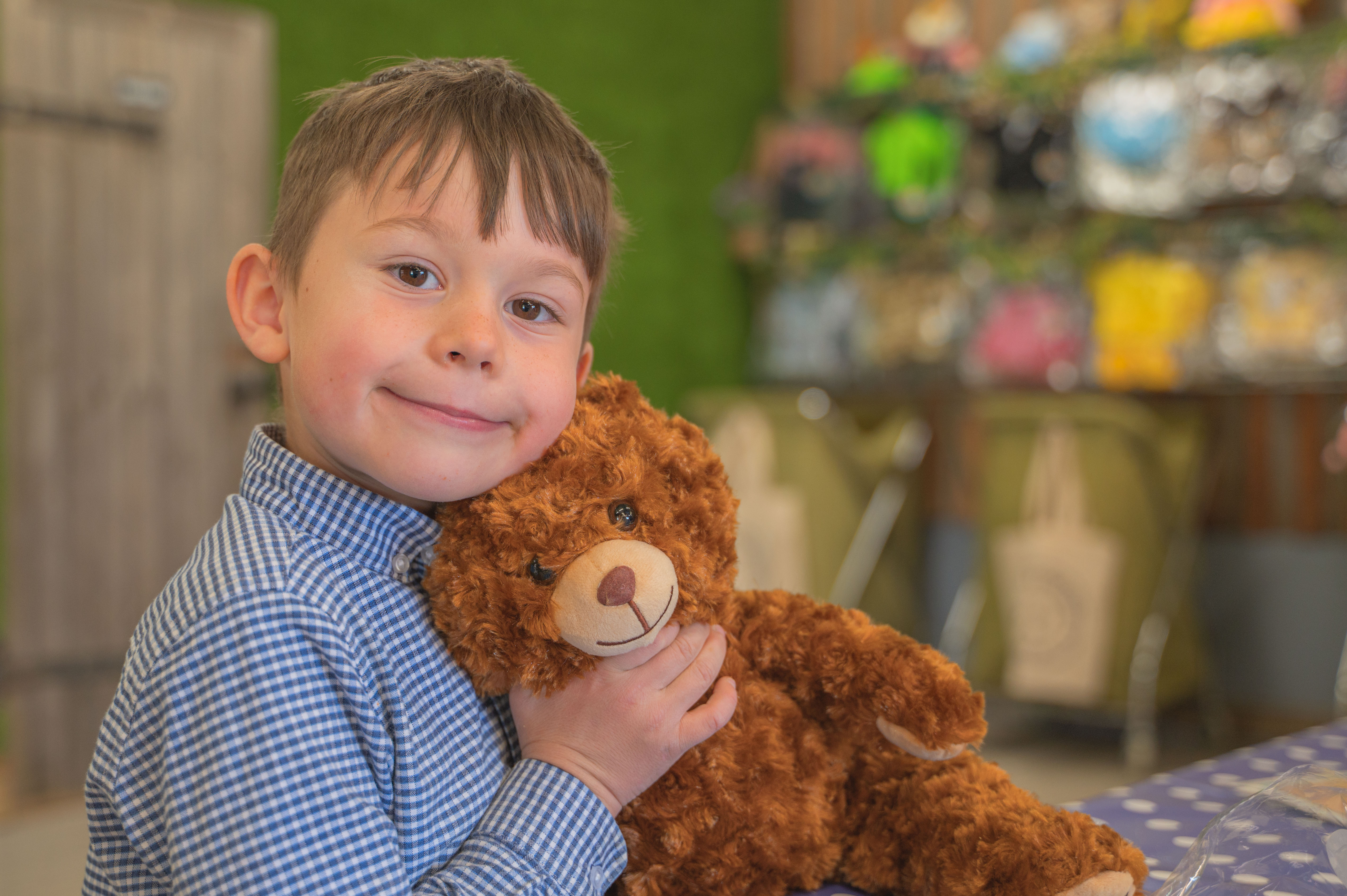 A young boy wearing a shirt with small blue checks with his teddy bear made at Cotswold Farm Park Easter on the Farm
