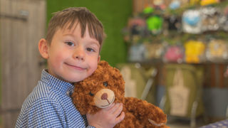 A young boy wearing a shirt with small blue checks with his teddy bear made at Cotswold Farm Park Easter on the Farm