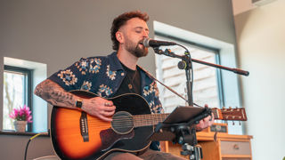 A male guitarist sits singing with a guitar in the Cotswold Farm Park Ox Shed