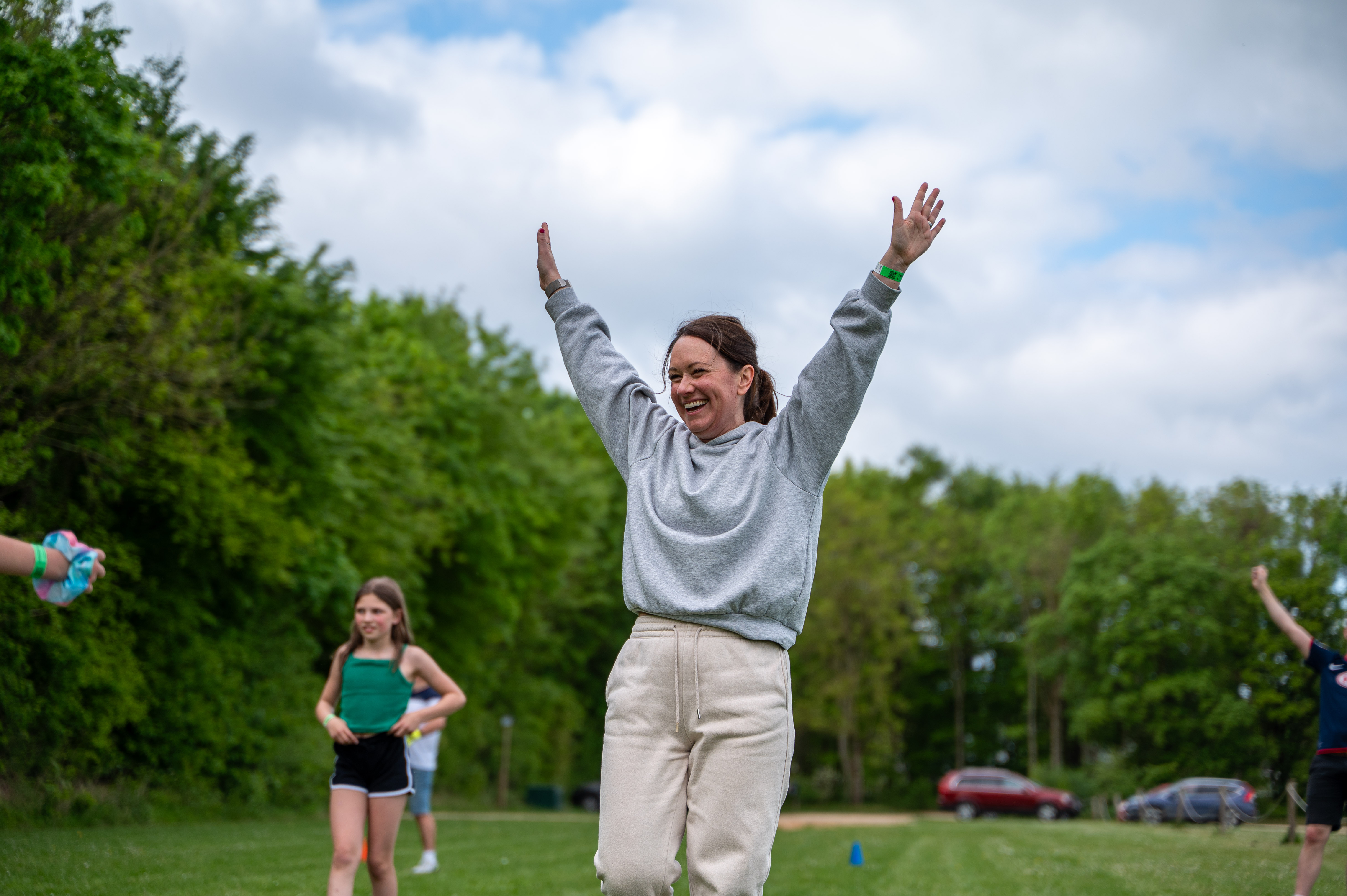 A lady stands on the recreation field at Cotswold Farm Park Holidays with her arms in the air celebrating a goal in a game of football