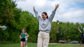 A lady stands on the recreation field at Cotswold Farm Park Holidays with her arms in the air celebrating a goal in a game of football