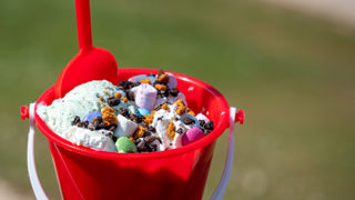 A red bucket and spade held up filled with ice cream with colourful toppings
