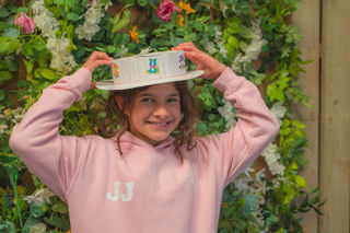 A girl wearing a pink hoodie holding her Easter bonnet, made at Cotswold Farm Park Easter on the Farm