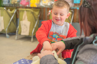 A small boy wearing a dinosaur shirt building a farm animal teddy bear at the Cotswold Farm Park Easter on the Farm