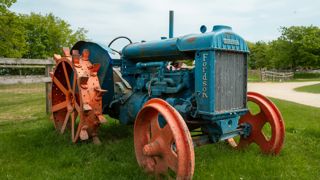 A vintage Fordson tractor, with rusted blue paintwork and red wheels sits on display at Cotswold Farm Park