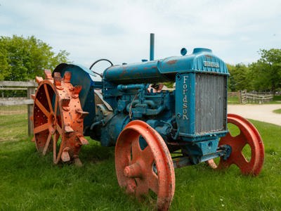 A vintage Fordson tractor, with rusted blue paintwork and red wheels sits on display at Cotswold Farm Park