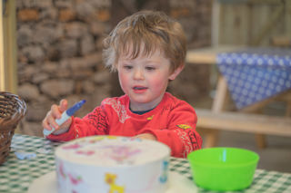 A small boy wearing a red top designing his own Easter bonnet with coloured markers at the Cotswold Farm Park Easter on the Farm