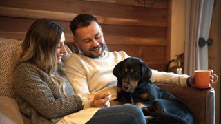 Couple on sofa smiling at black medium-sized dog