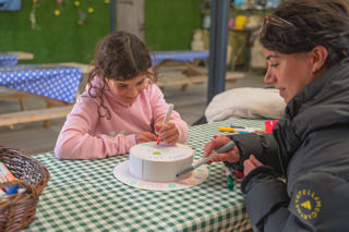 A girl and her mum colouring a cardboard Easter bonnet at Cotswold Farm Park Easter on the Farm on a checked tablecloth