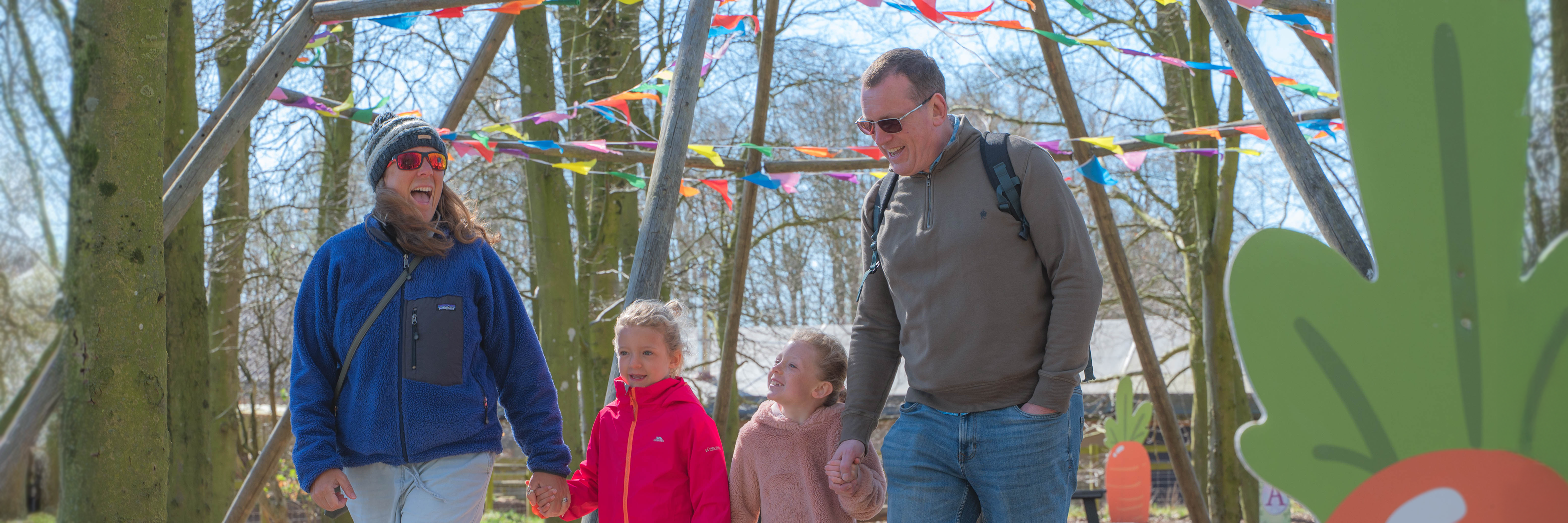 A family of 4 with walking through woodland at Cotswold Farm Park on an Easter egg hunt